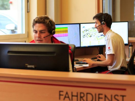 Two Austrian Red Cross dispatchers in headsets coordinating patient transport at the Fahrdienst dispatch desk